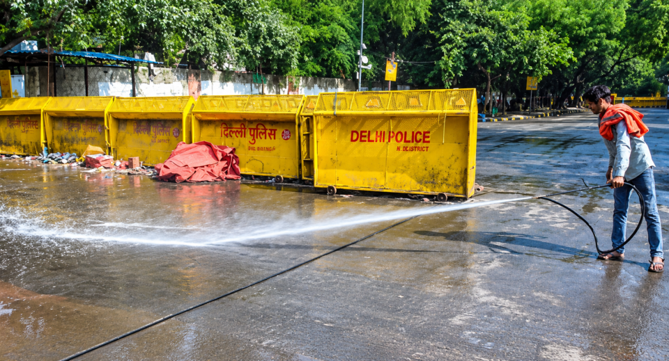 Delhi Police barricades on a New Delhi road as a worker washes the pavement with water.