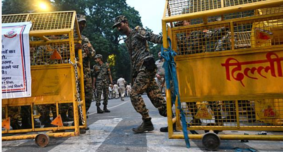 Delhi Police security barricades with uniformed security personnel standing on duty on a city road.